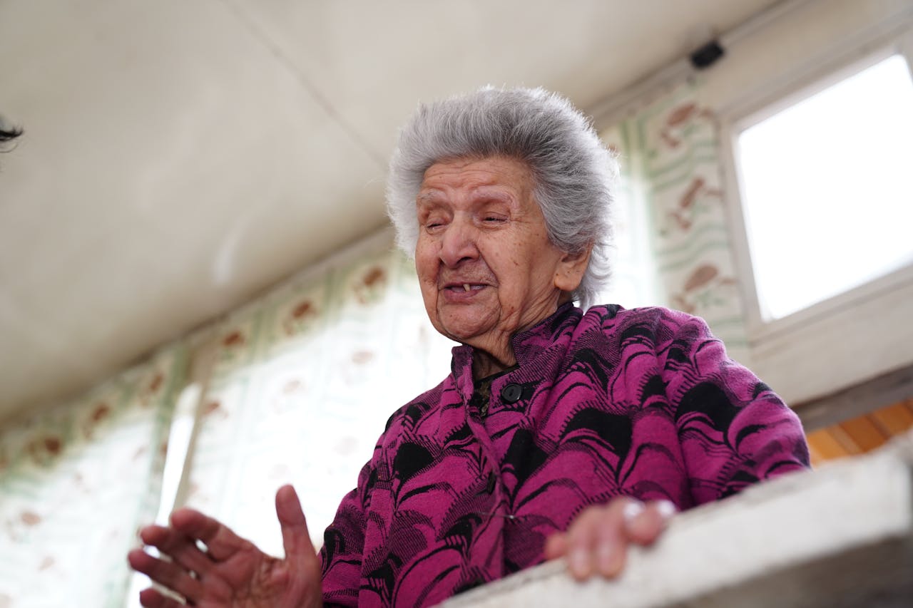 A joyful senior woman indoors, wearing a vibrant sweater, expressing happiness.